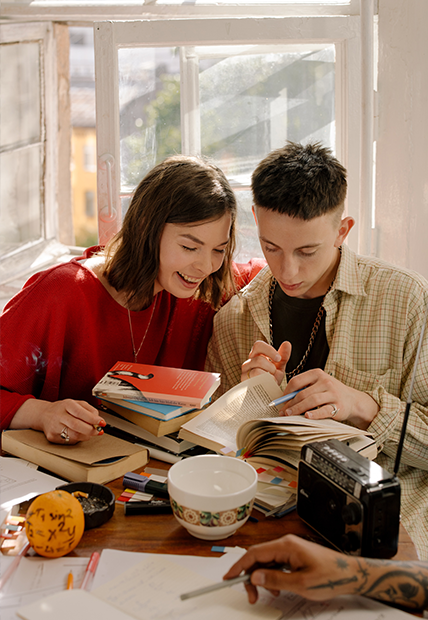 Two students looking through books around a coffee table