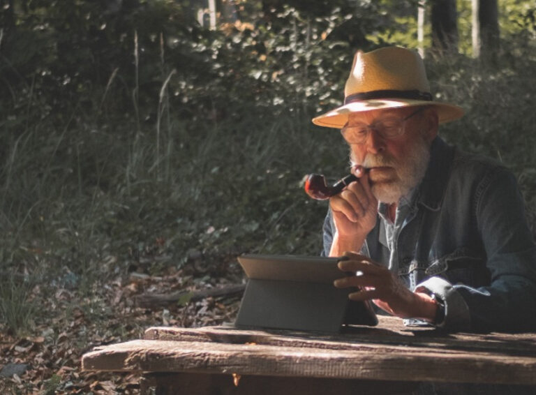 An older male sits on a tablet in a forest.