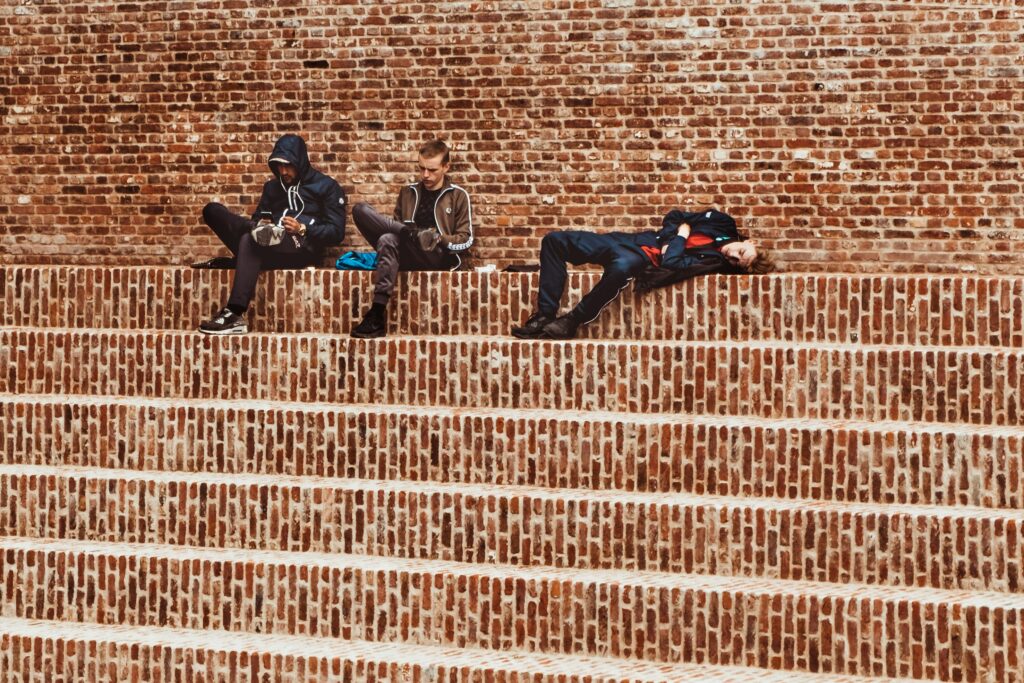 three young men sit on a staircase, two on phones. 
