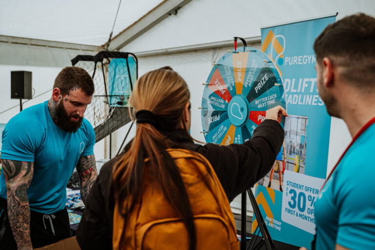 University students at a freshers fair stall spinning a wheel to win a free PureGym prize.