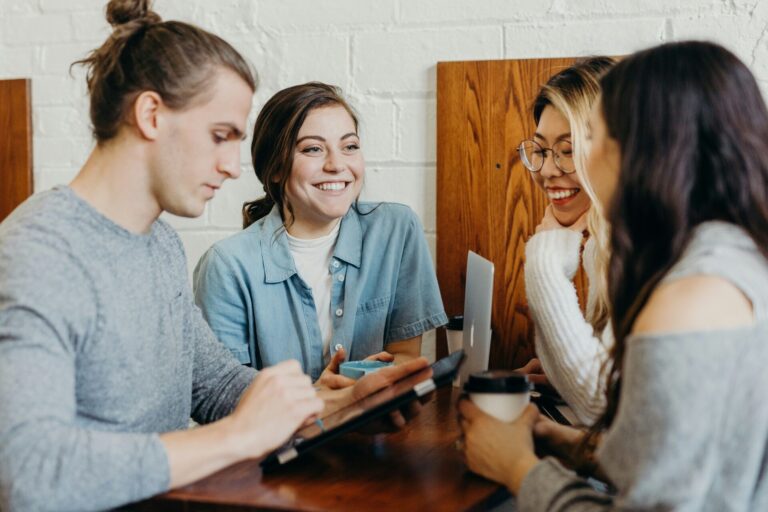 A group of young friends at a coffee shop browsing on a device.