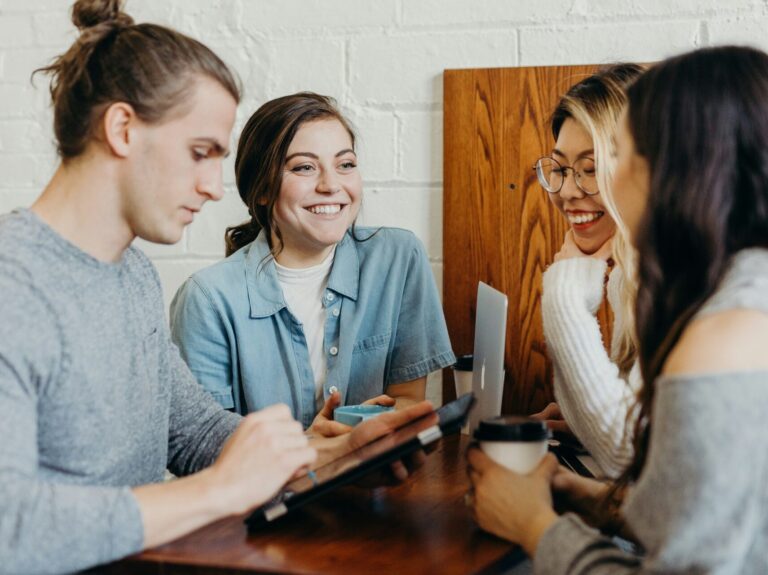 A group of young friends at a coffee shop browsing on a device.